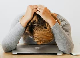 A woman in gray long sleeves resting her head on a laptop, appearing tired or stressed